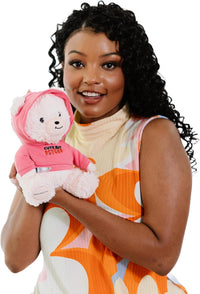A woman in a colorful dress holds the Punchkins 🐻 "Cute But PSYCHO" 😈 Teddy Bear Plushie w/ Bloody Kitchen Knife 🩸—a sassy white teddy in a pink hoodie, perfect for adding charm and edgy humor to any occasion.