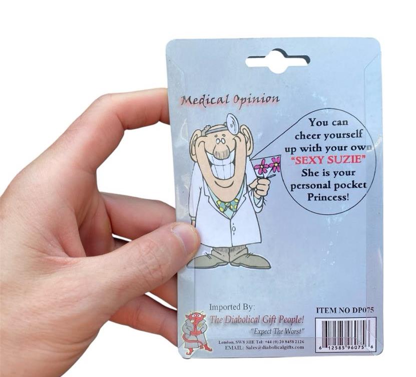A hand holds packaging with a cartoon doctor and drink, promoting the "Saucy Suzie Flashing Stripper Keychain"—a funny adult peepshow toy that’s the perfect gag gift and playful pocket-sized companion.