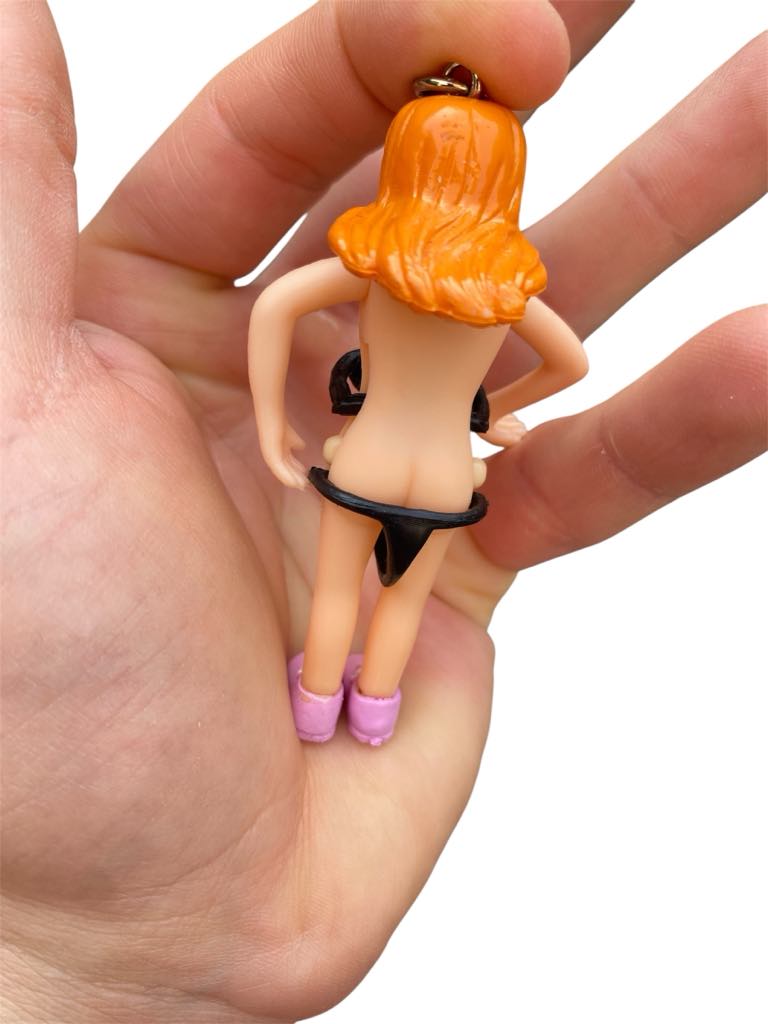 A hand holds the Saucy Suzie Flashing Stripper Keychain—a funny adult gag gift showing a woman with orange hair pulling down her black skirt and wearing pink shoes, viewed from the back.