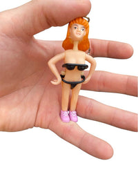 A hand holds the Saucy Suzie Flashing Stripper Keychain—a funny adult gag gift peepshow toy featuring a woman with orange hair, black bikini, and pink shoes—set against a white background.