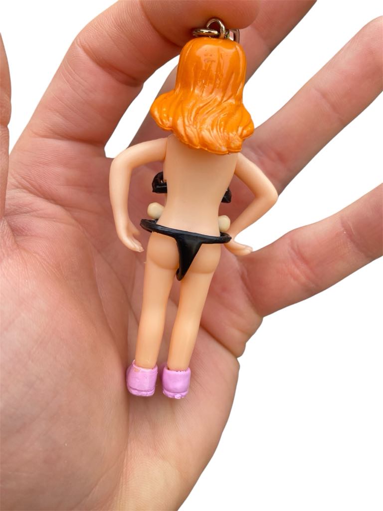 A hand holds the Saucy Suzie Flashing Stripper Keychain—a funny adult gag gift peepshow toy featuring a plastic figure with orange hair, black underwear, and pink shoes, shown from the back.
