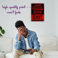 A person relaxes on the couch, game controller in hand, chuckling at the humorous Metal Tin Sign "Game Controller THROW ZONE" Bedroom Gamer Wall Decor #F-101 displayed on the wall.