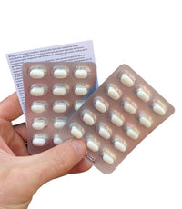 A hand holds two blister packs of white oval tablets labeled Trumptacs Mints – Funny Donald Trump Candy Box of 30 with a leaflet behind them—funny presidential mints to Make Breath Great Again or give as quirky gag gifts.