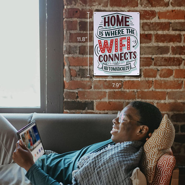 A person relaxes on a couch using a tablet while the Metal Tin Sign "Home is Where the WIFI Connects Automatically" Wall Decor #H-101 hangs above them. This delightful piece of home decor also serves as an ideal gift for any tech-savvy friend.