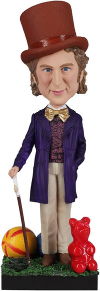 The Willy Wonka Bobblehead Statue – Gene Wilder Collectible Figure by Royal Bobbles features Willy in a purple coat with cane, standing beside a red gummy bear and colorful ball on a grassy base.