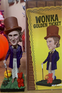 The Willy Wonka Bobblehead Statue – Gene Wilder Collectible Figure by Royal Bobbles🍬 features Wonka in his purple coat and top hat, next to "Wonka Golden Ticket" packaging, complete with cane, balloons, and golden egg.