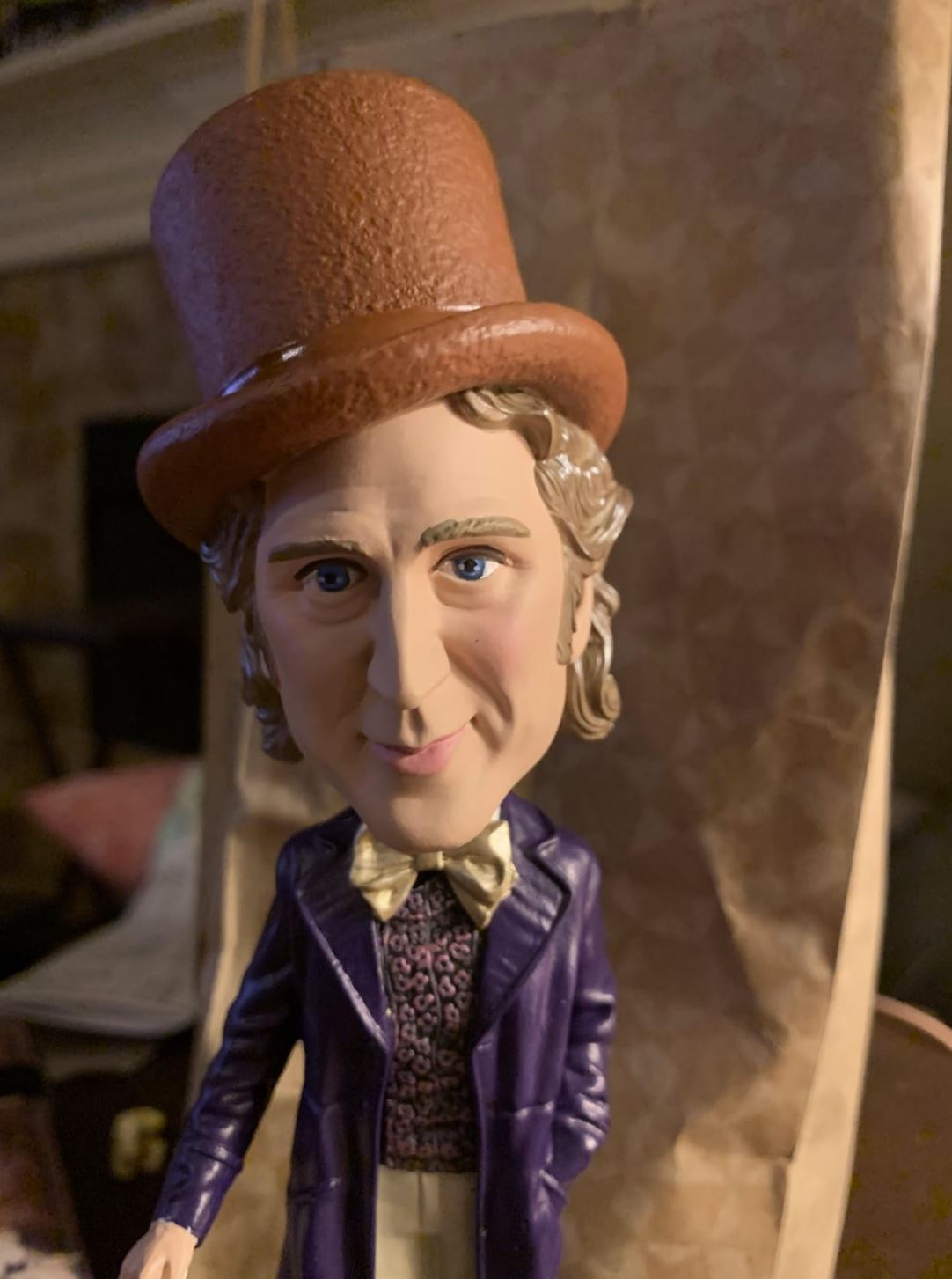 The Willy Wonka Bobblehead Statue – Gene Wilder Collectible Figure by Royal Bobbles🍬 features a hand-painted Willy in a brown top hat, purple coat, and bow tie against a patterned backdrop—a whimsical collectible.
